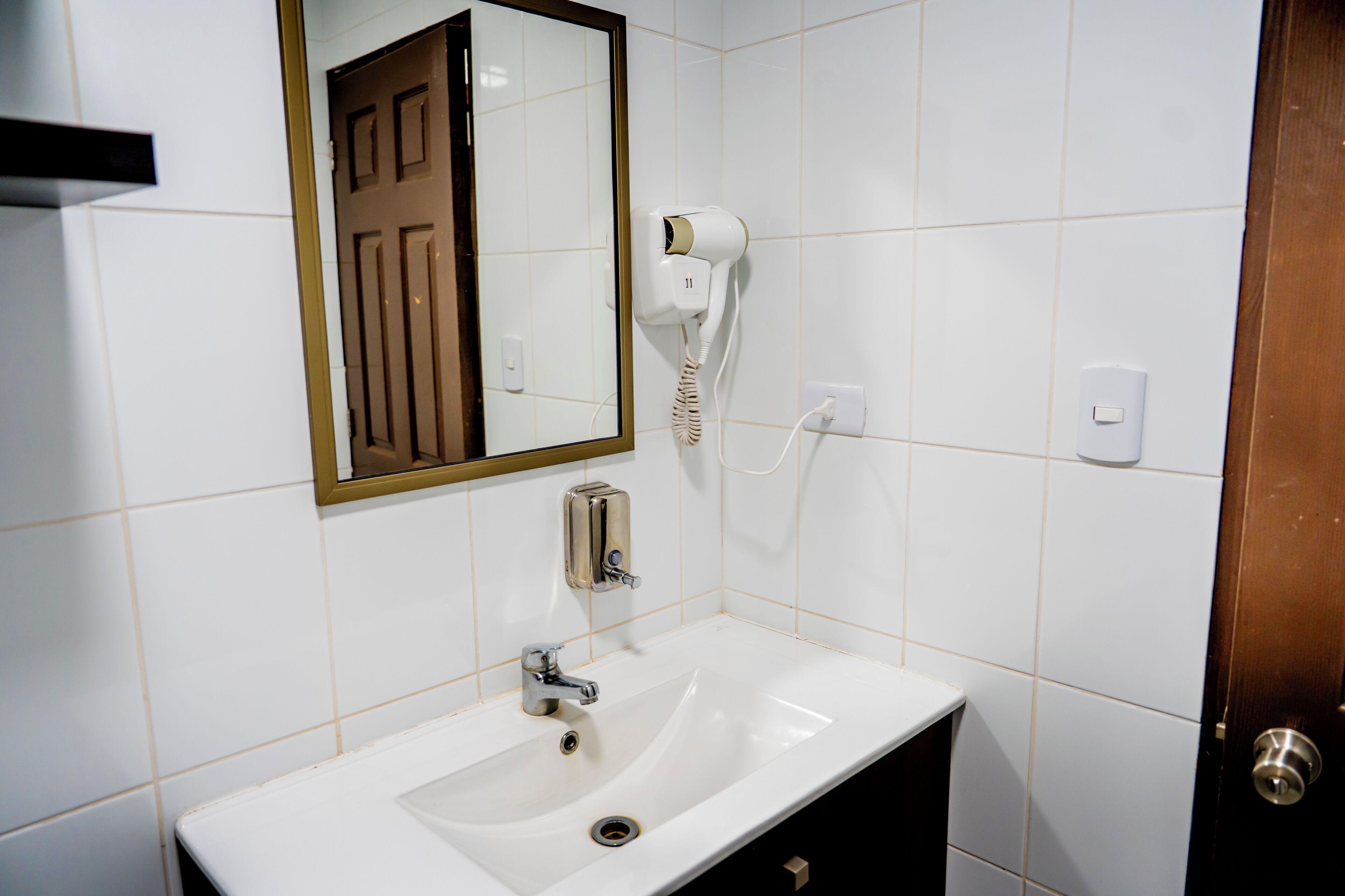 Un baño con lavamanos blanco, secador de pelo, espejo y puerta.
