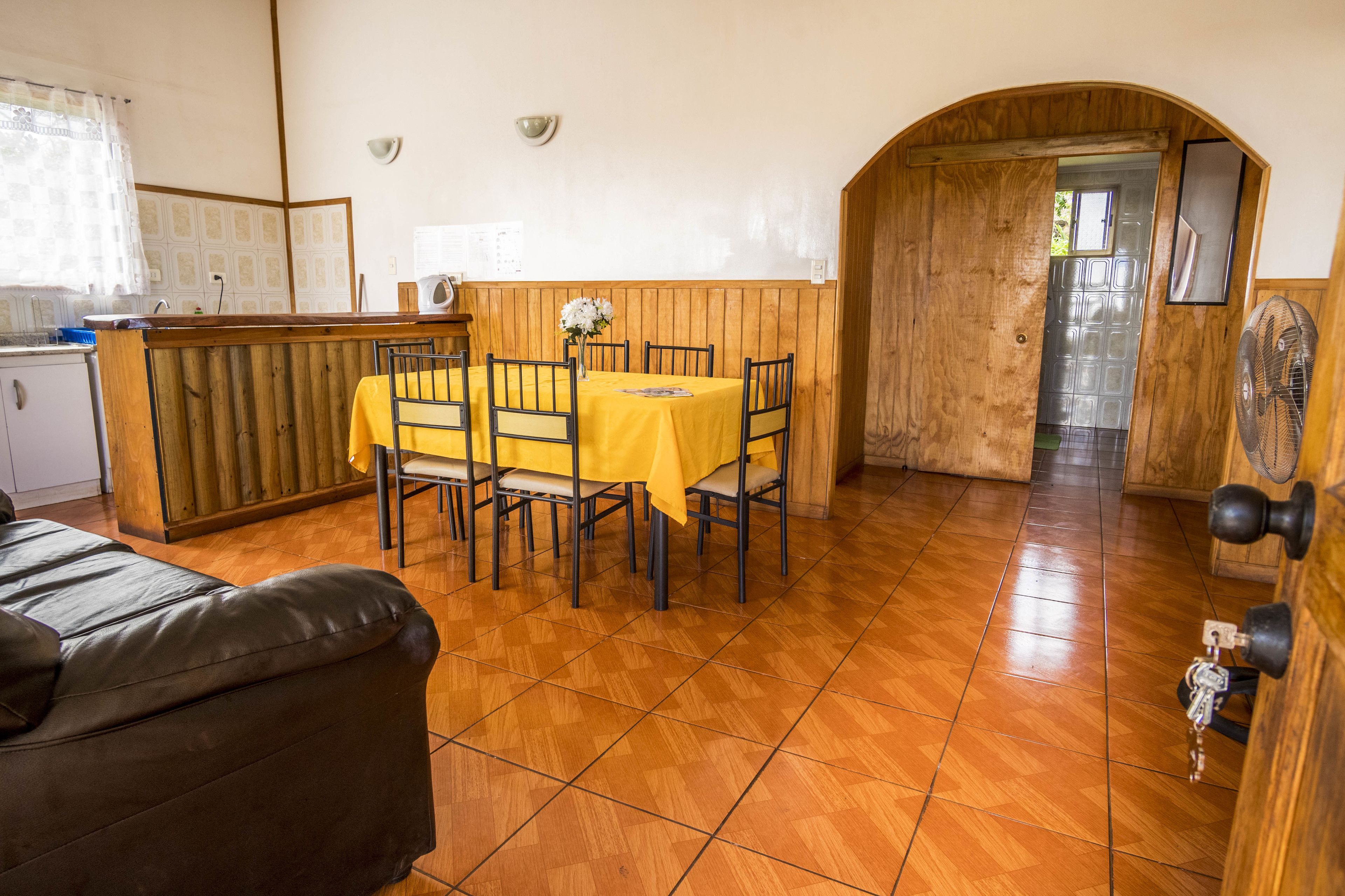 Un comedor con una mesa y sillas de madera, una cocina con un refrigerador blanco y una puerta de madera que da a otra habitación.