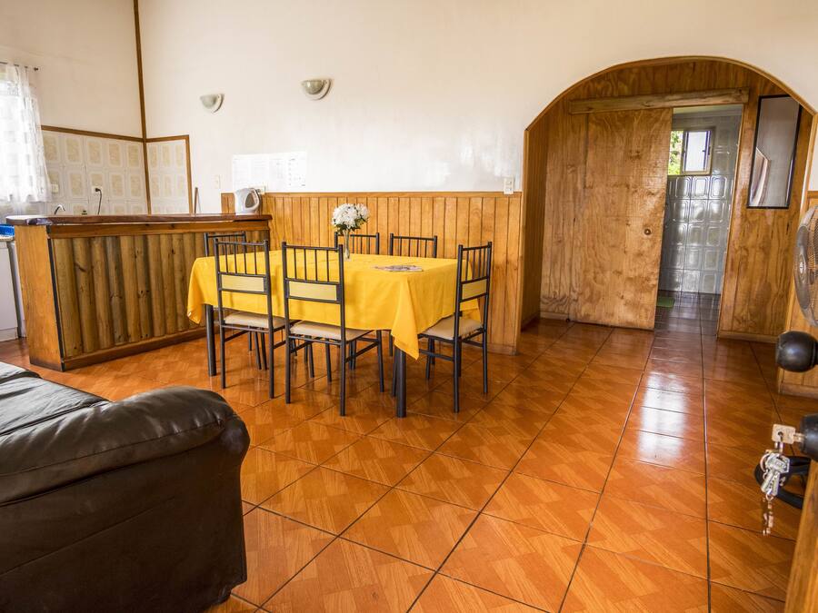 Un comedor con una mesa y sillas de madera, una cocina con un refrigerador blanco y una puerta de madera que da a otra habitación.