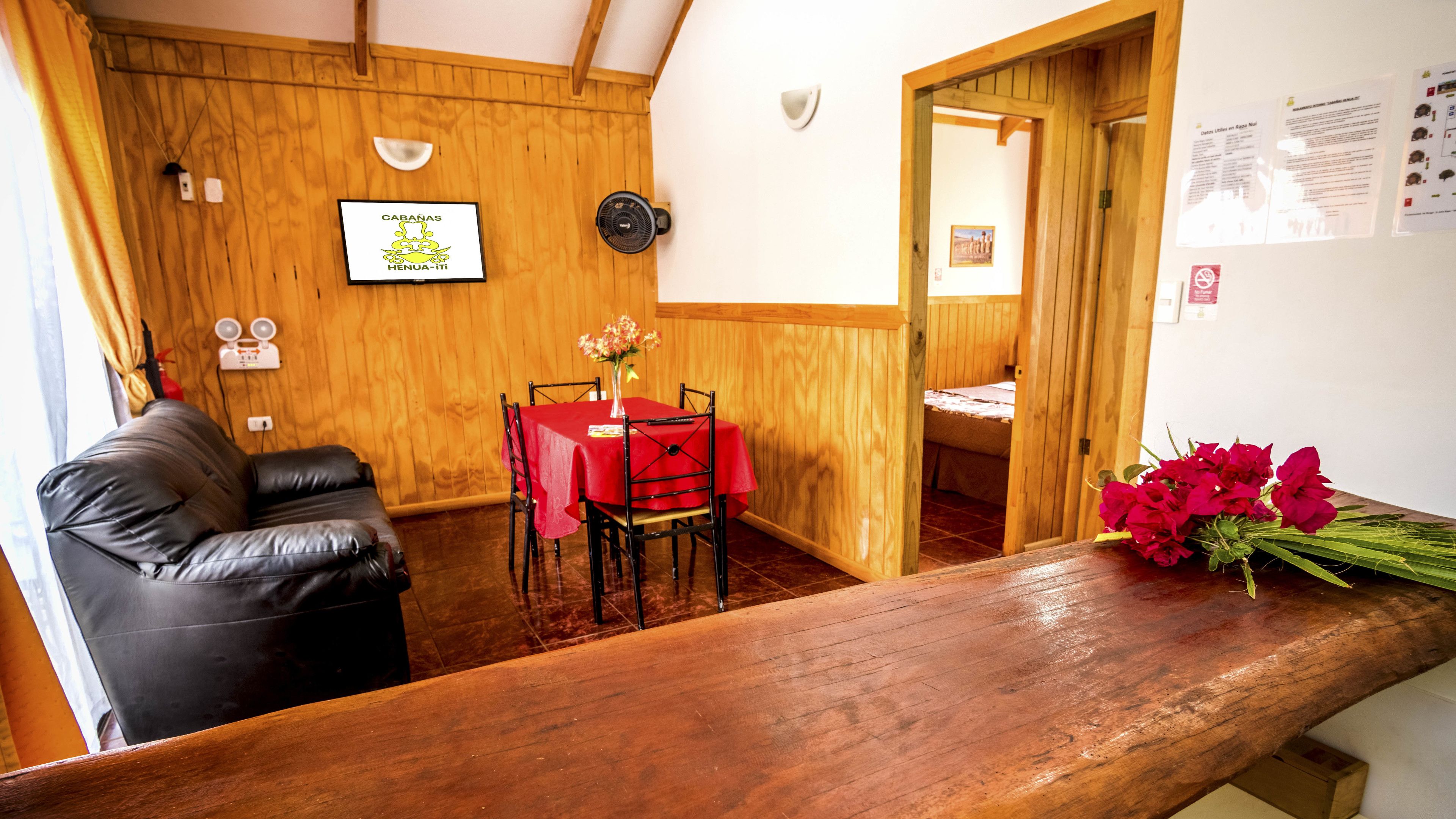 A wooden interior with a dining table set for two, a leather sofa, and a wooden counter with a bouquet of flowers.