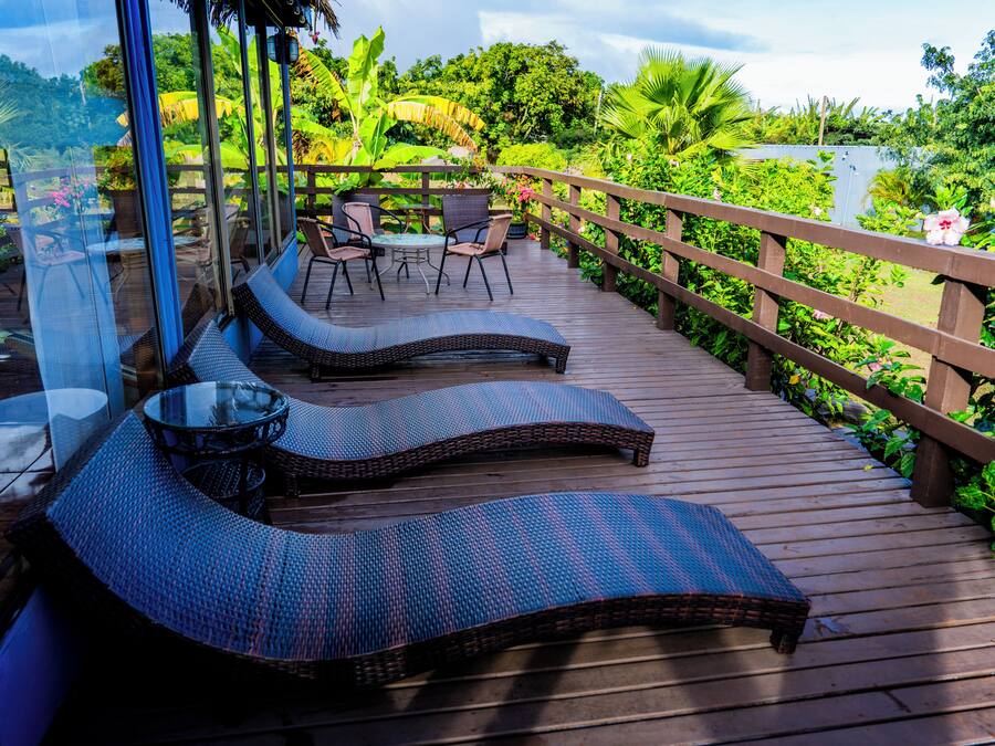 A wooden deck with lounge chairs and a table, surrounded by lush greenery and a wooden railing.
