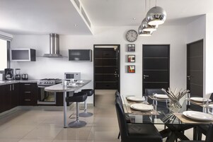 Una cocina moderna con comedor, que incluye electrodomésticos de acero inoxidable, armarios negros y una mesa de vidrio.