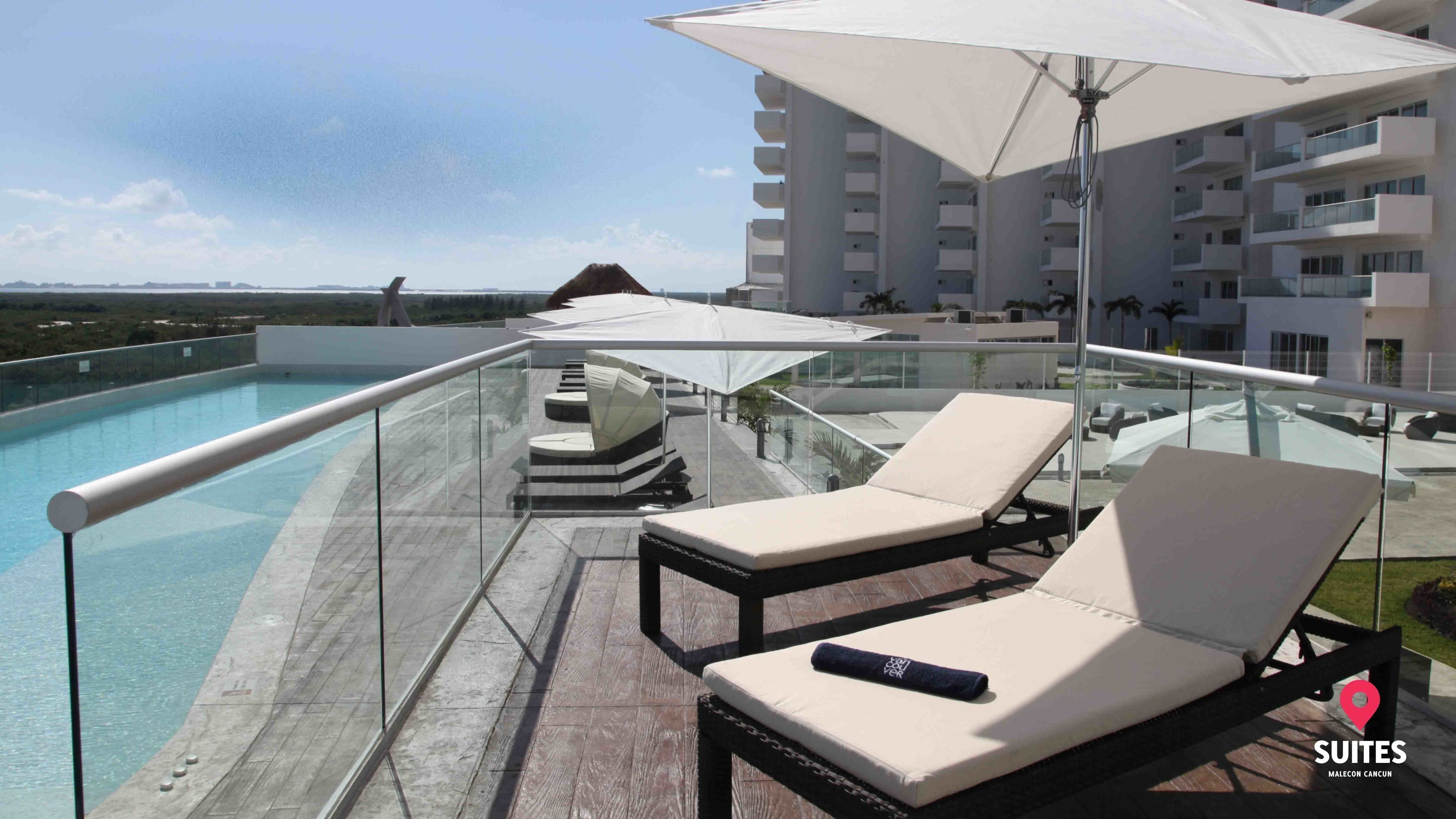 Area piscina sul tetto con due lettini, ringhiera in vetro e vista sull'oceano e sugli edifici.