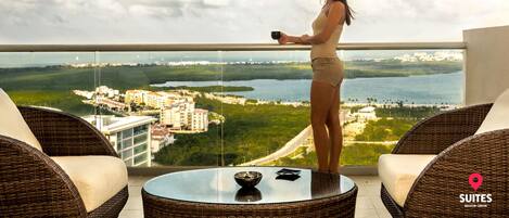 A woman standing on a balcony overlooking a coastal cityscape with buildings and water.