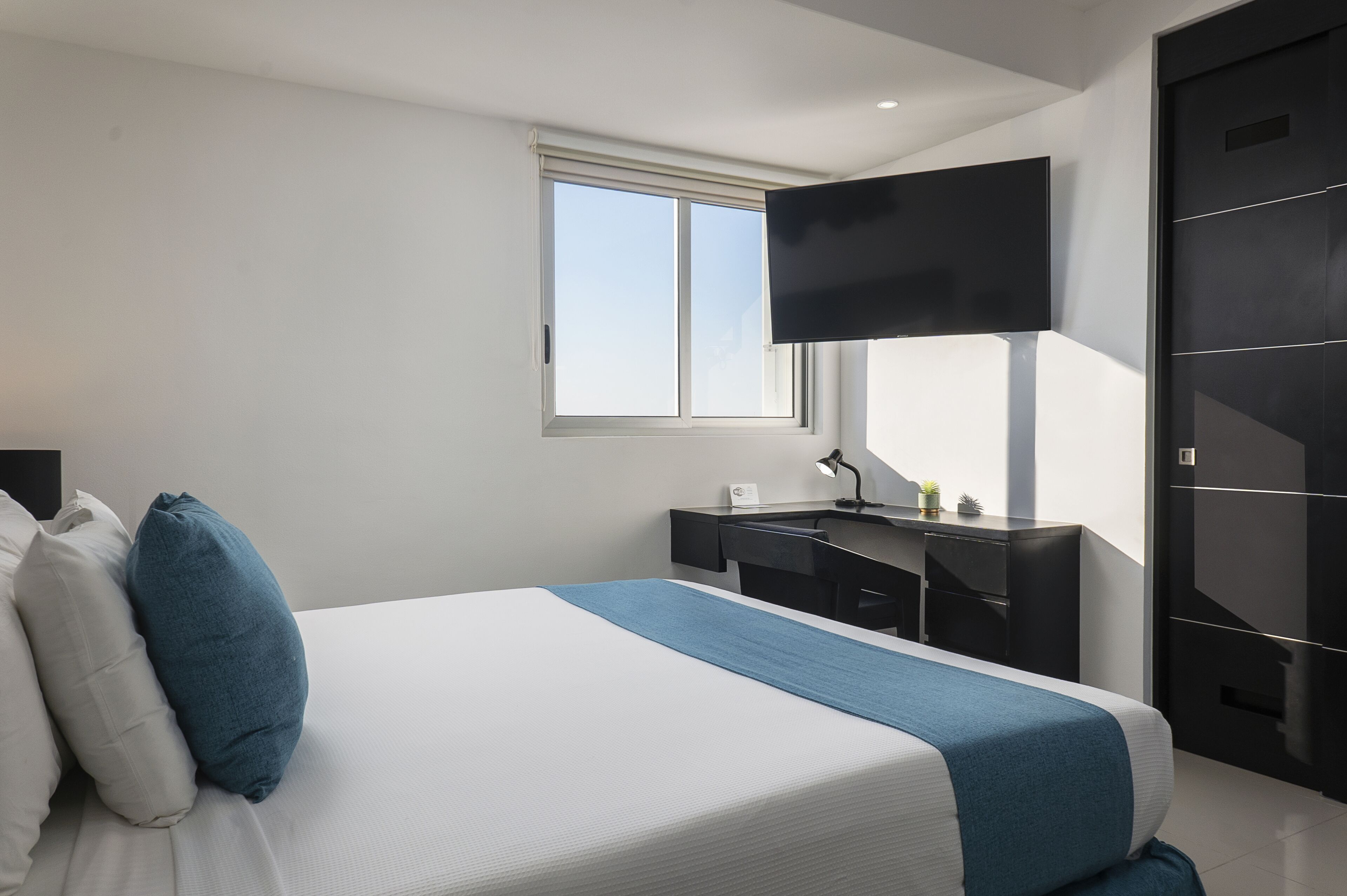 Una habitación de hotel moderna con una cama grande, un escritorio y un televisor montado en la pared.