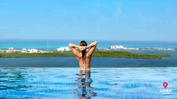 A person in a swimming pool with a view of the ocean and distant buildings. - Suites Malecon Cancun (Cancun)