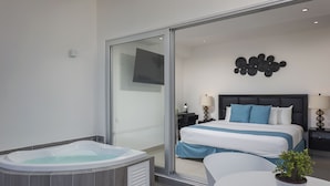 A modern hotel room with a large bed, a glass shower enclosure, a jacuzzi, and a small table with a potted plant. - Suites Malecon Cancun (Cancun)