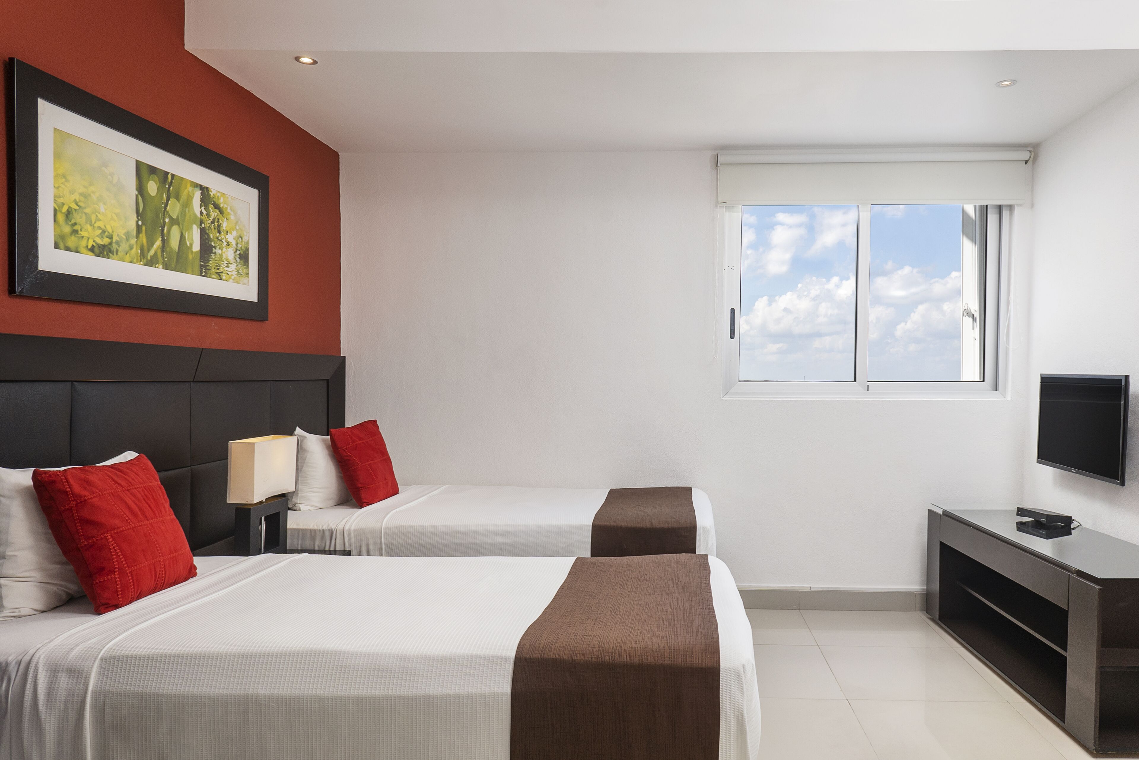 A hotel room with two beds, a TV, a window with a view, and a painting on the wall.