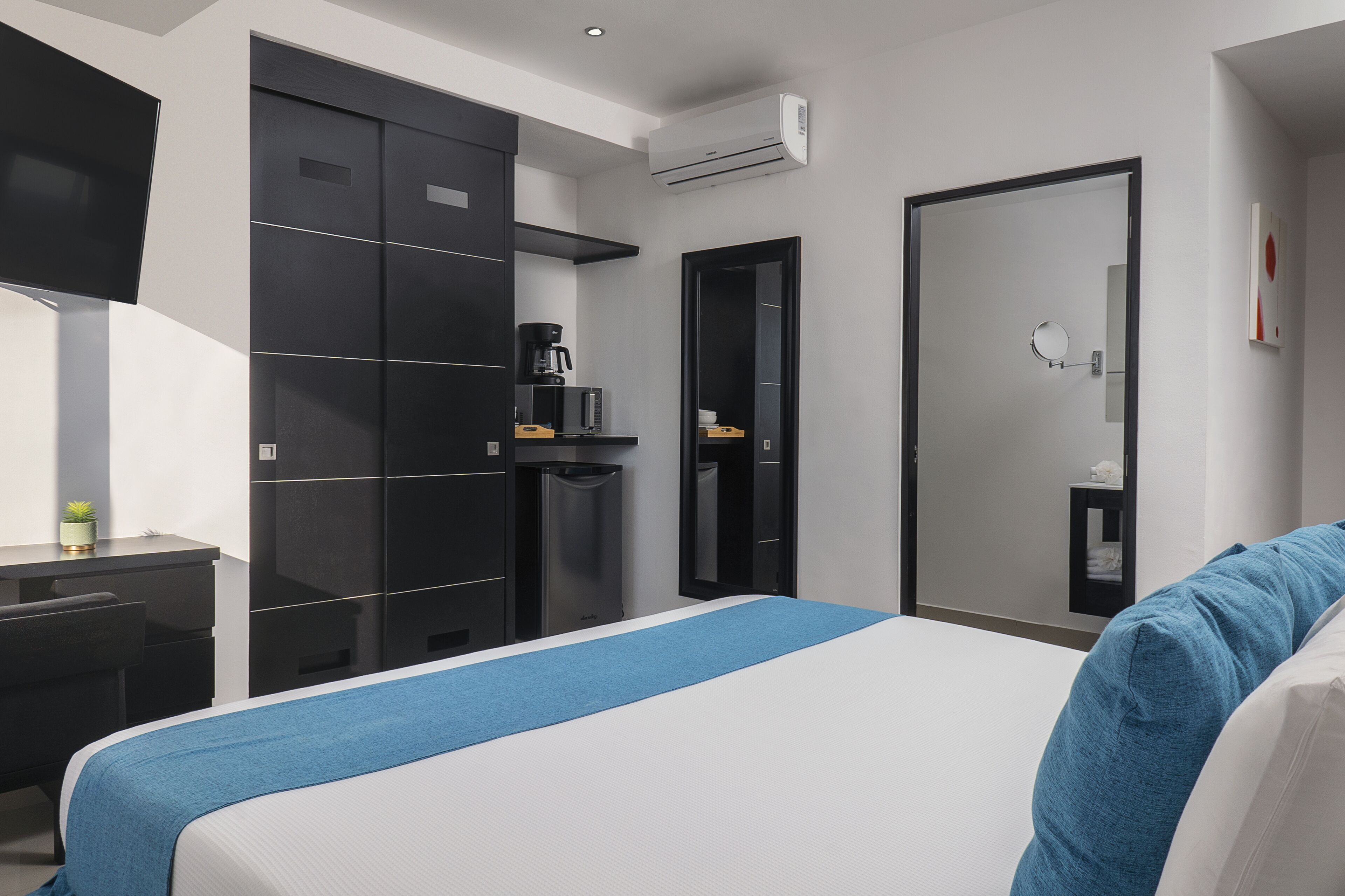 Moderni hotellihuone, jossa on suuri sänky, työpöytä, vaatekaappi ja peili.