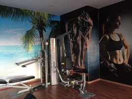 Un gimnasio con equipo de ejercicio, un mural en la pared de una figura musculosa y vistas al océano.