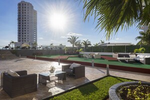 A rooftop lounge with outdoor furniture, a green artificial turf area, and a tall building in the background.