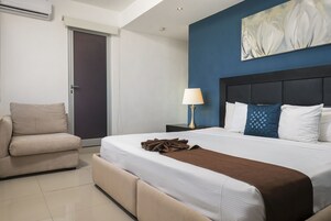 Una habitación de hotel con cama, sofá, mesita de noche con lámpara y puerta.