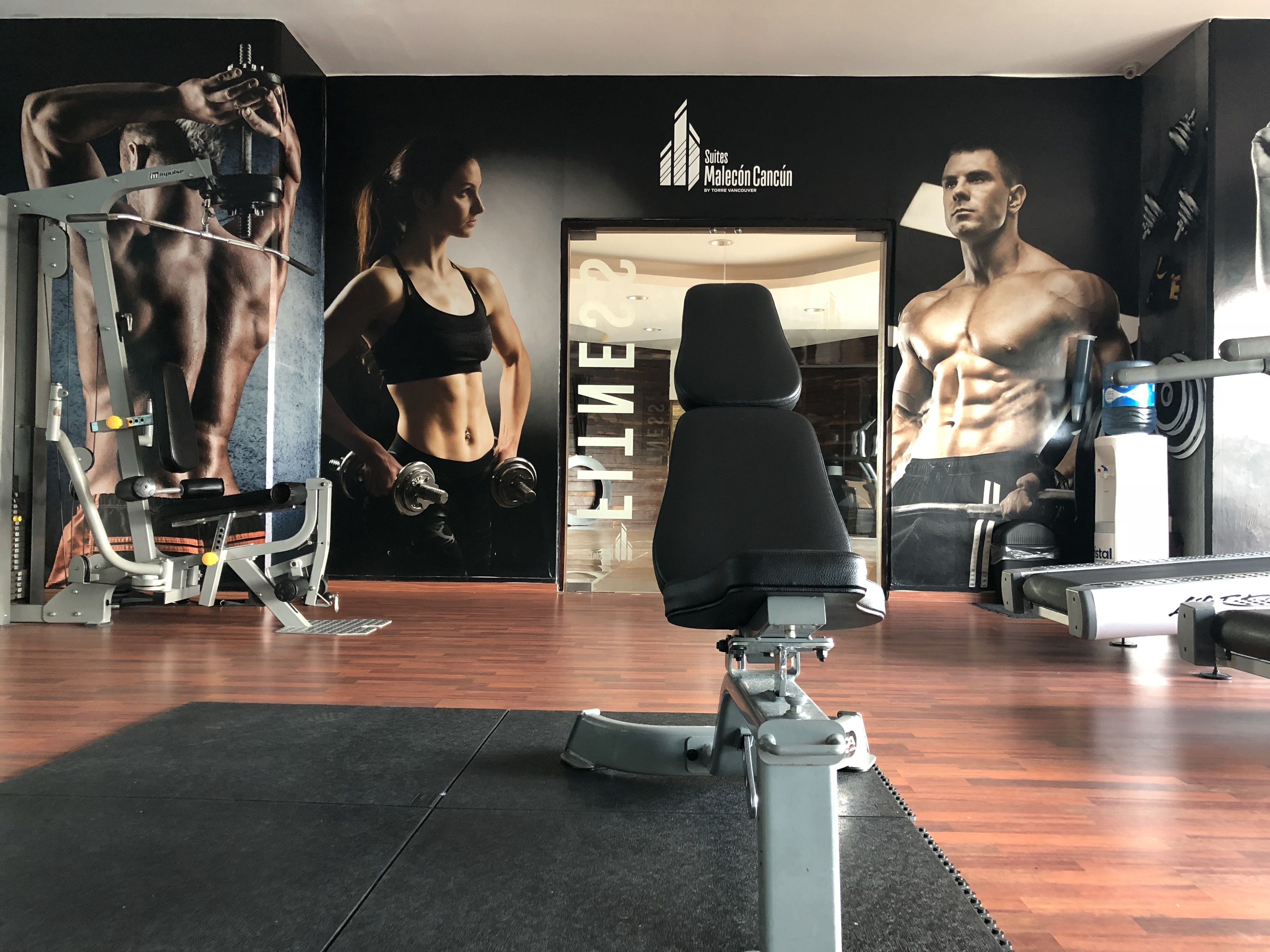 Een sportschool met trainingsapparatuur, een spiegel en posters van modellen.
