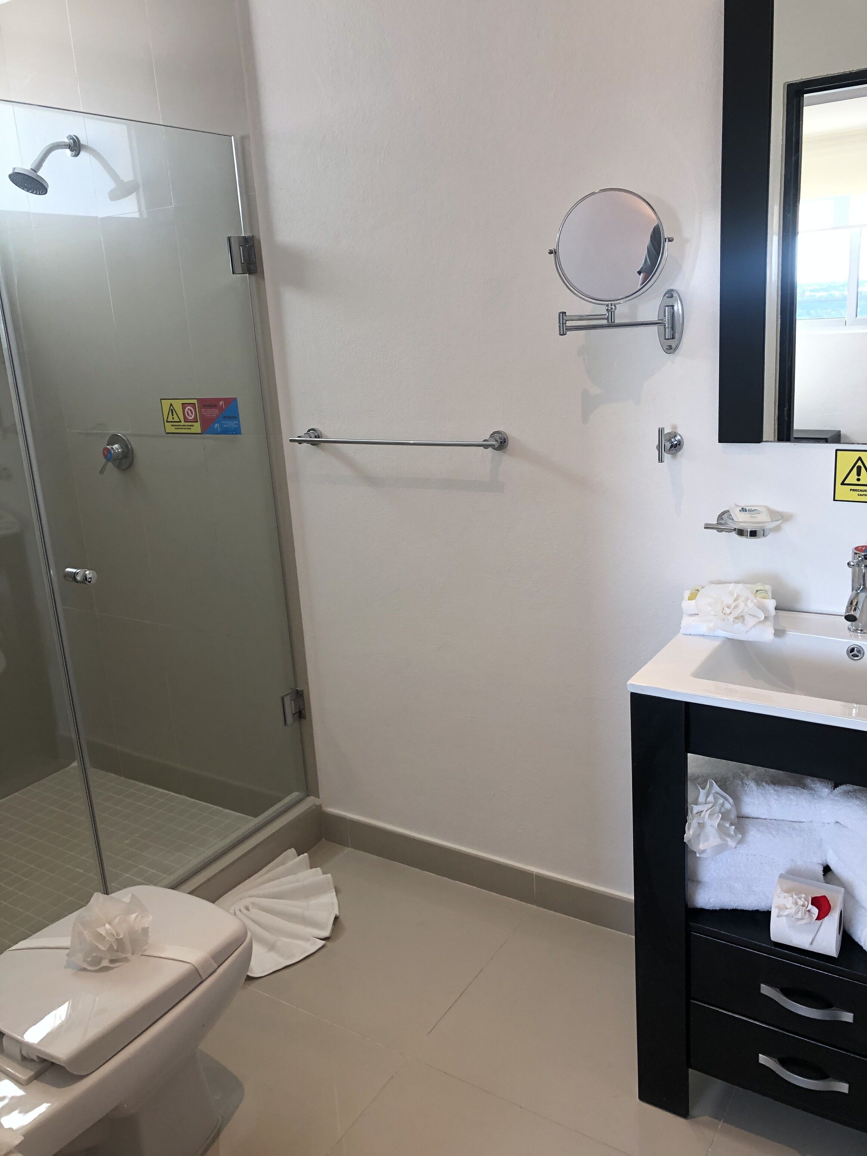 Un baño con cabina de ducha de vidrio, inodoro, lavabo con espejo y perchero para toallas.