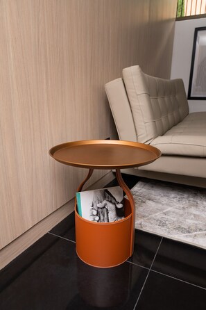 A modern living room with a beige sofa, a small round table with a leather top, and a brown leather basket with magazines. - Hotel Zona A (Medellín)