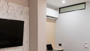 A modern living room with a flat-screen TV mounted on a marble wall, a wooden desk with a laptop, a black chair, and a patterned rug. - Hotel Zona A (Medellín)