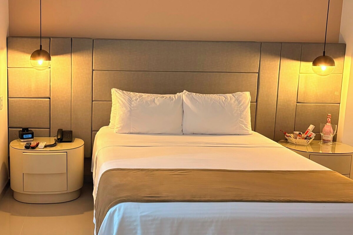 A hotel room with a bed, bedside tables, and two pendant lights.