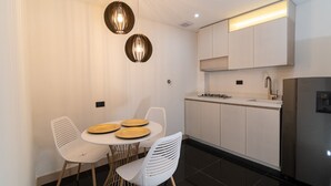 A modern kitchen with white cabinets, a stainless steel refrigerator, and a dining area with a round table and chairs. - Hotel Zona A (Medellín)