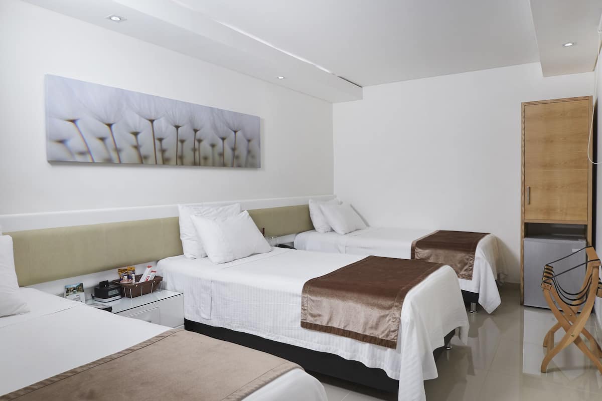 Habitación de hotel con dos camas, un armario de madera, una mesita con lámpara y una obra de arte colgada en la pared.