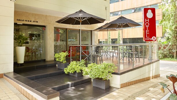 A hotel entrance with a glass facade, outdoor seating area, and potted plants. - Hotel Zona A (MedellĂn)