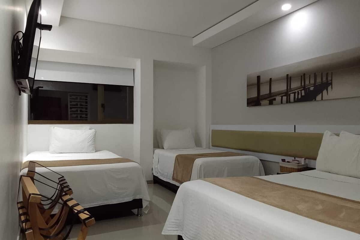 Habitación de hotel con dos camas, un televisor de pantalla plana montado en la pared y una ventana con persianas.