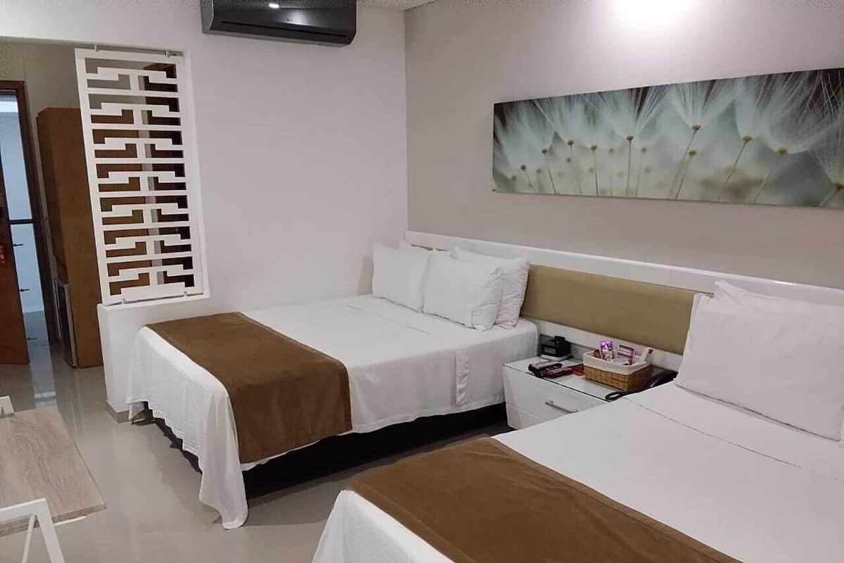 Una habitación de hotel con dos camas, una mesita de noche, aire acondicionado de pared y un adorno en la pared.