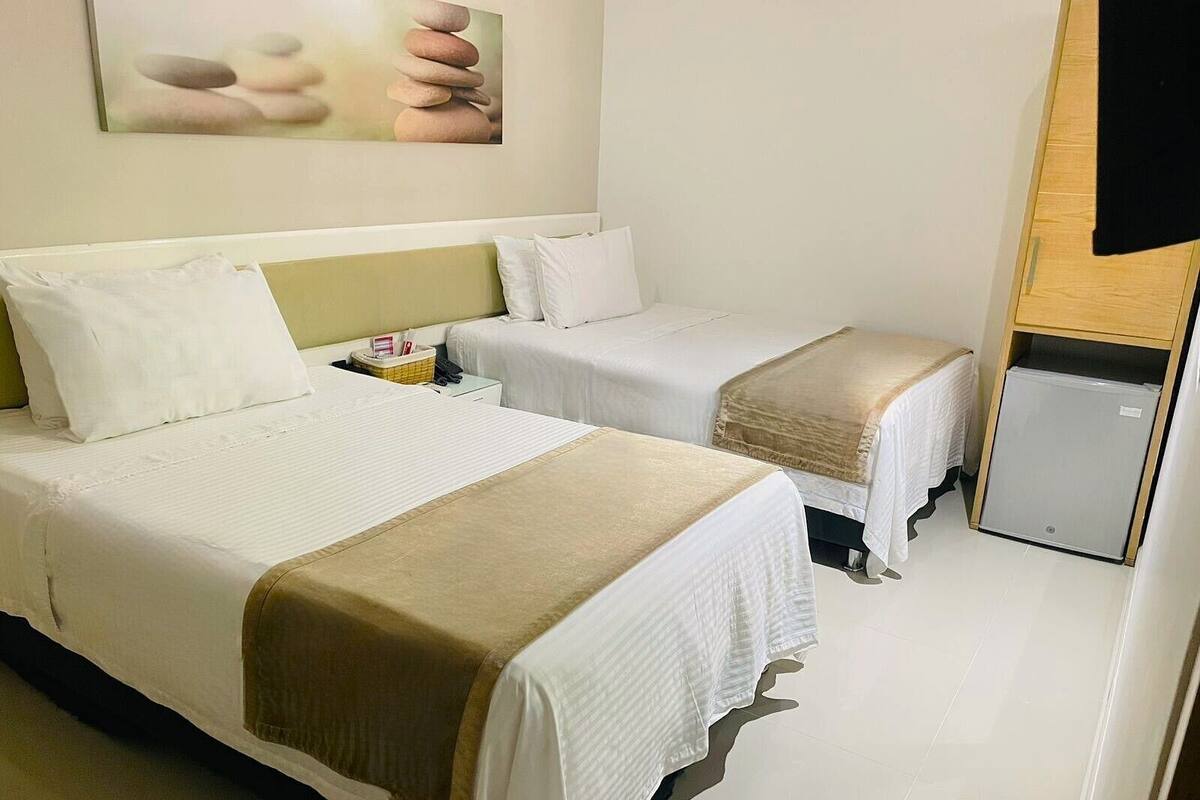 Habitación de hotel con dos camas, un refrigerador pequeño y un cuadro en la pared.