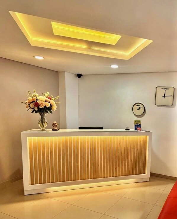 A reception desk with a clock and a wall clock, a vase of flowers, and a ceiling light fixture. - Hotel Zona A (Medellín)