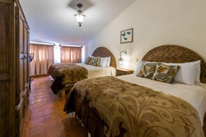 Habitación de hotel con dos camas, un armario de madera, un ventilador de techo y una lámpara fijada a la pared.