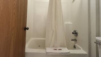 A bathtub with a white shower curtain, a towel, and a wooden door.