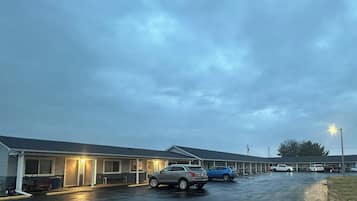 Um motel com uma fileira de quartos, um estacionamento e o chão encharcado, provavelmente por causa da chuva recente.