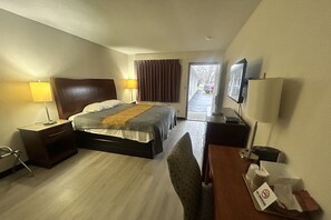 A hotel room with a bed, bedside tables, a desk, a chair, a TV, and a window with curtains.