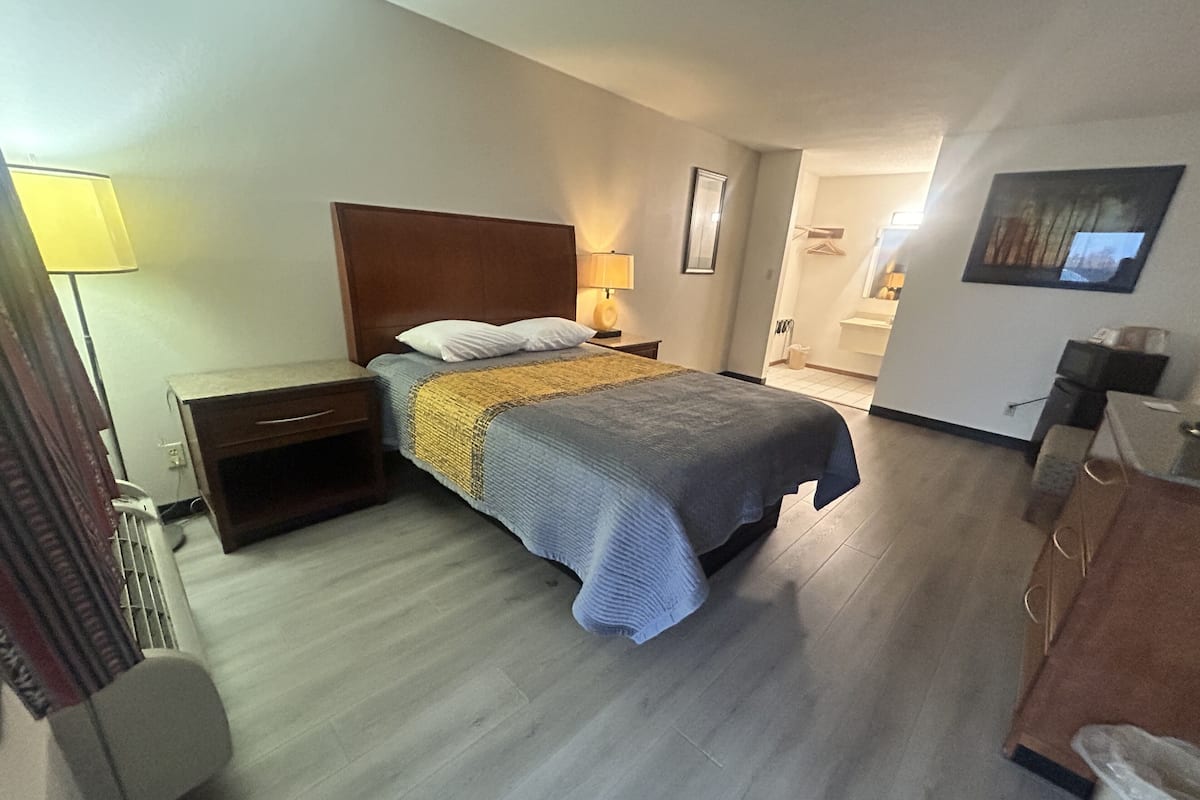 Hotellihuone, jossa on sänky, yöpöytä, lamppu ja taustalla näkyy kylpyhuone.