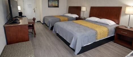 Habitación de hotel con dos camas, un escritorio, una silla, un televisor y un cuadro en la pared.