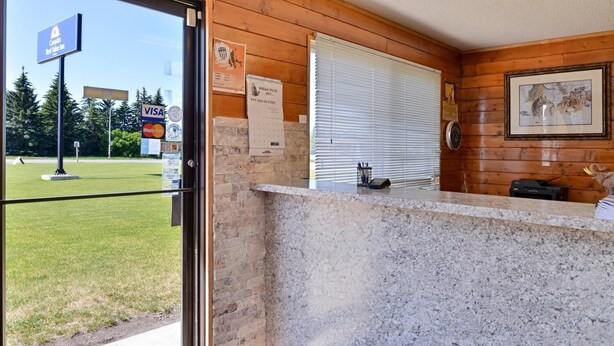 A reception desk with a wooden interior, a window with blinds, and a framed picture on the wall. - Motel 8 (Olds)