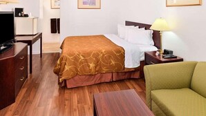 A hotel room with a wooden floor, a bed with a brown and white bedspread, a green armchair, a desk with a lamp, and a television. - Motel 8 (Olds)