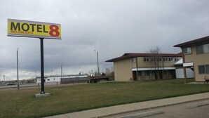A motel named 'Motel 8' with a large sign, a parking lot, and a building with a flat roof and multiple windows. - Motel 8 (Olds)