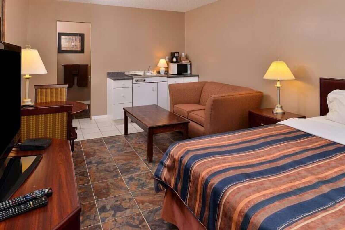 A hotel room with a bed, a desk, a chair, a television, and a kitchenette.