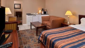 Habitación de hotel con cama, escritorio, silla, televisor y kitchenette.