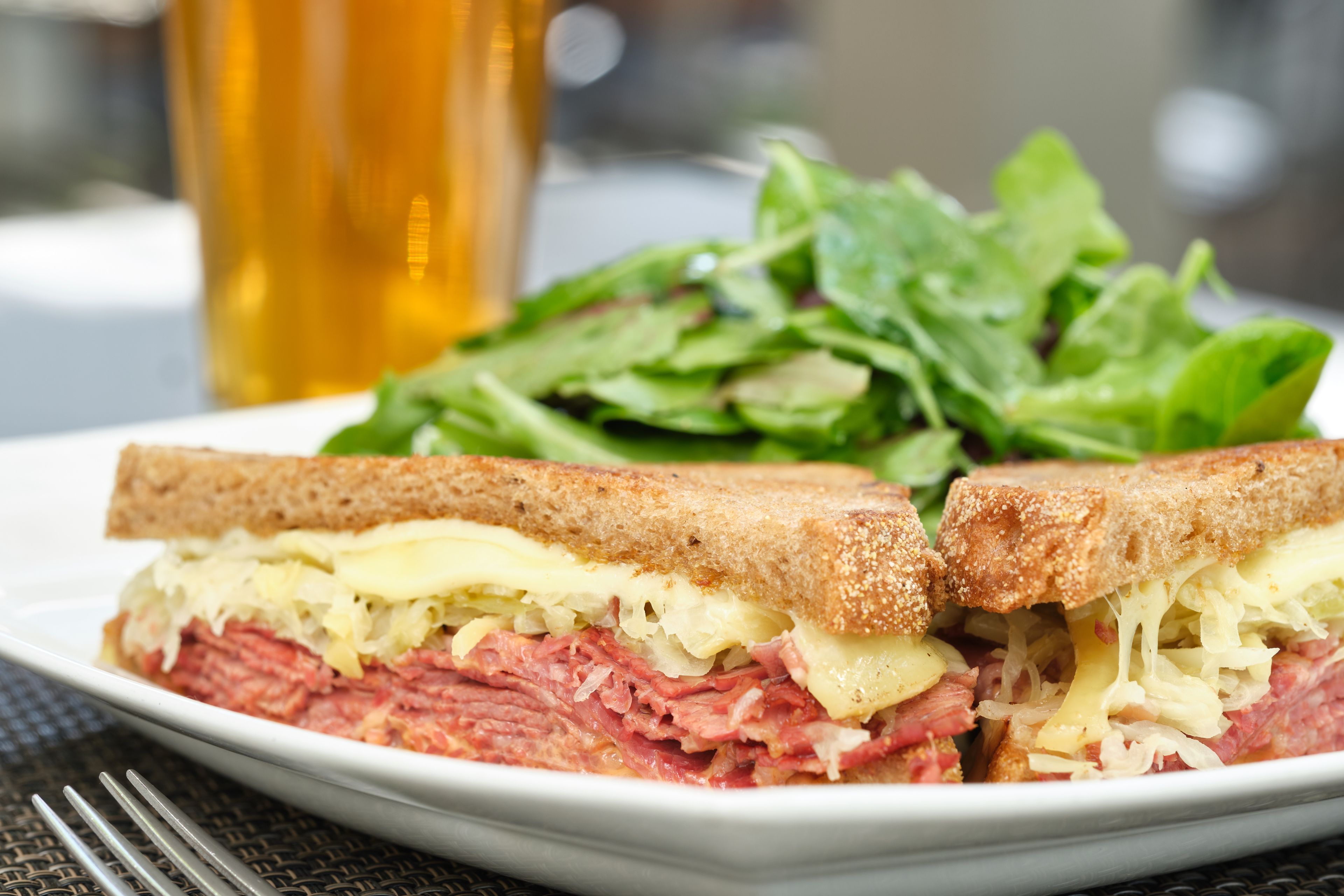 En sandwich med en salat og et glas øl på en tallerken.