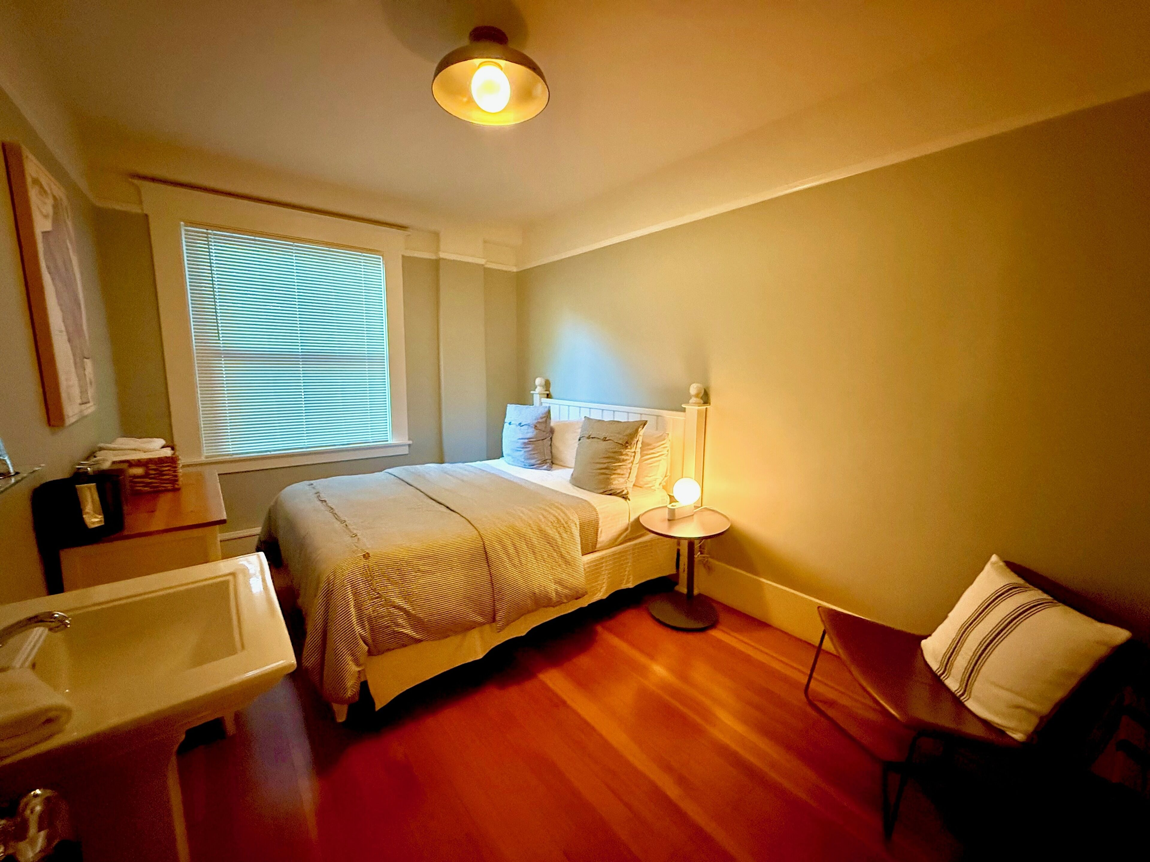 A bedroom with a bed, bedside table, lamp, and a window with blinds.