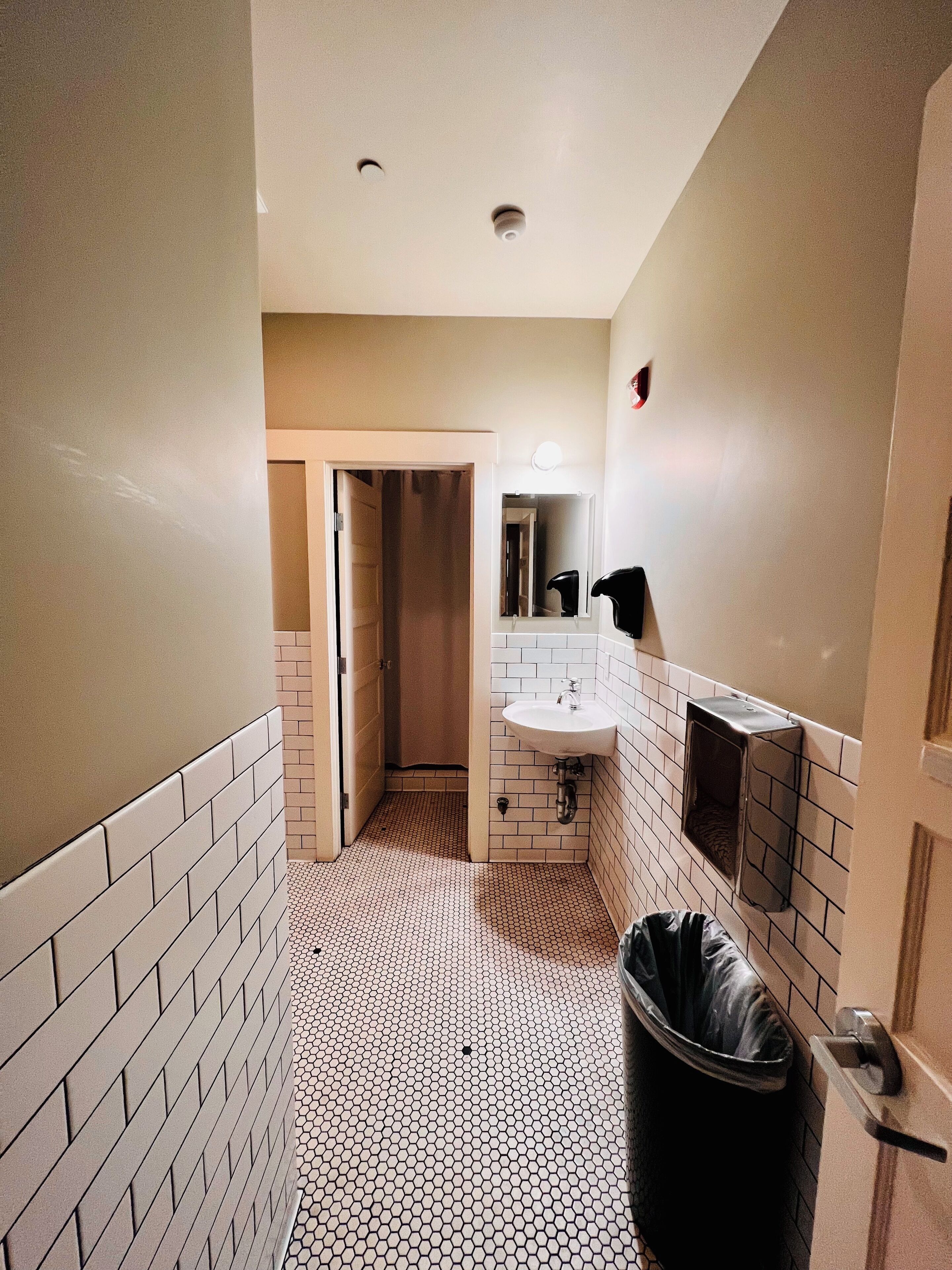 Un couloir étroit avec un sol carrelé, un lavabo et une poubelle.