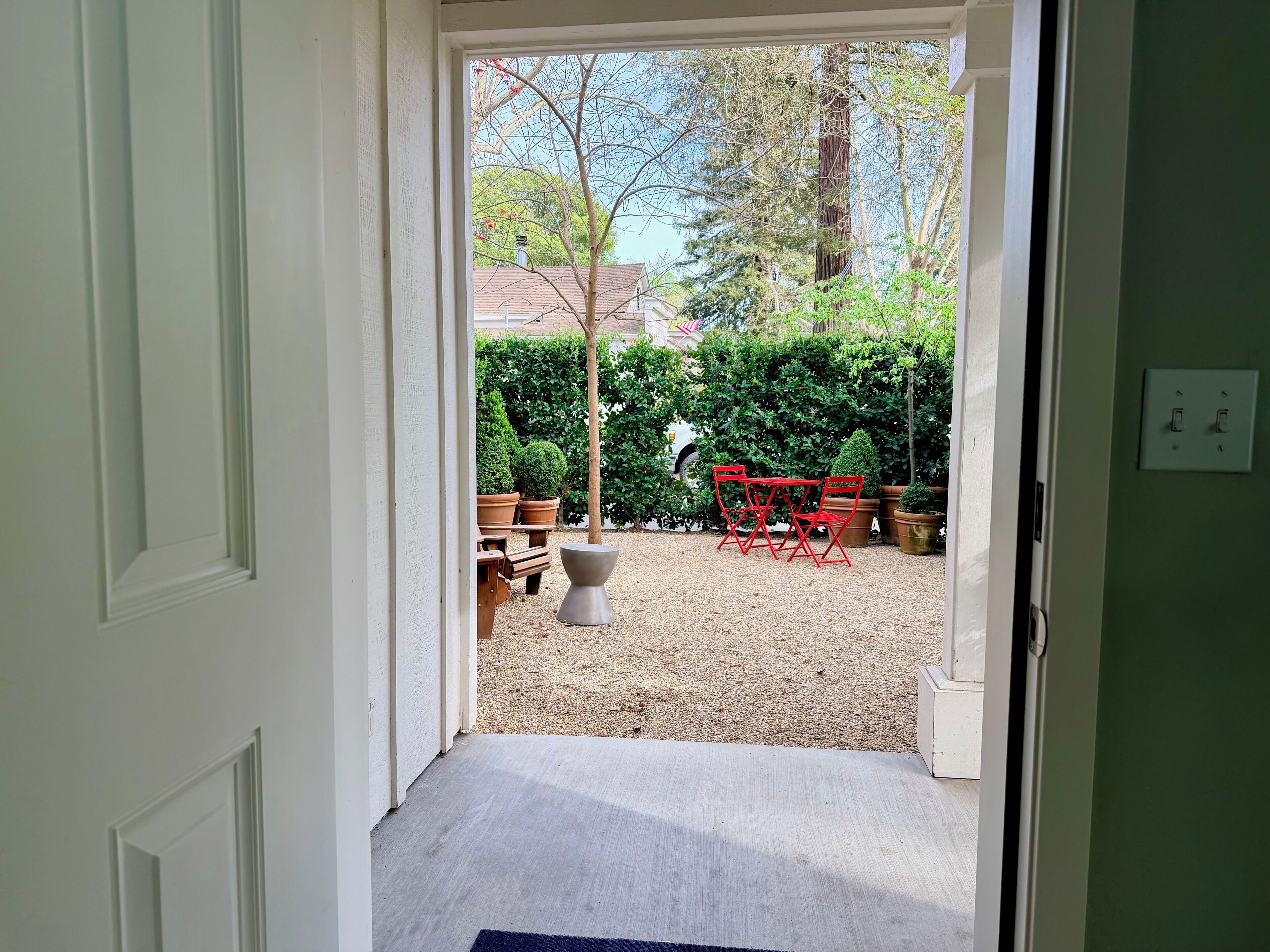 A doorway leading to a backyard with a gravel area, a red table and chairs, and potted plants.