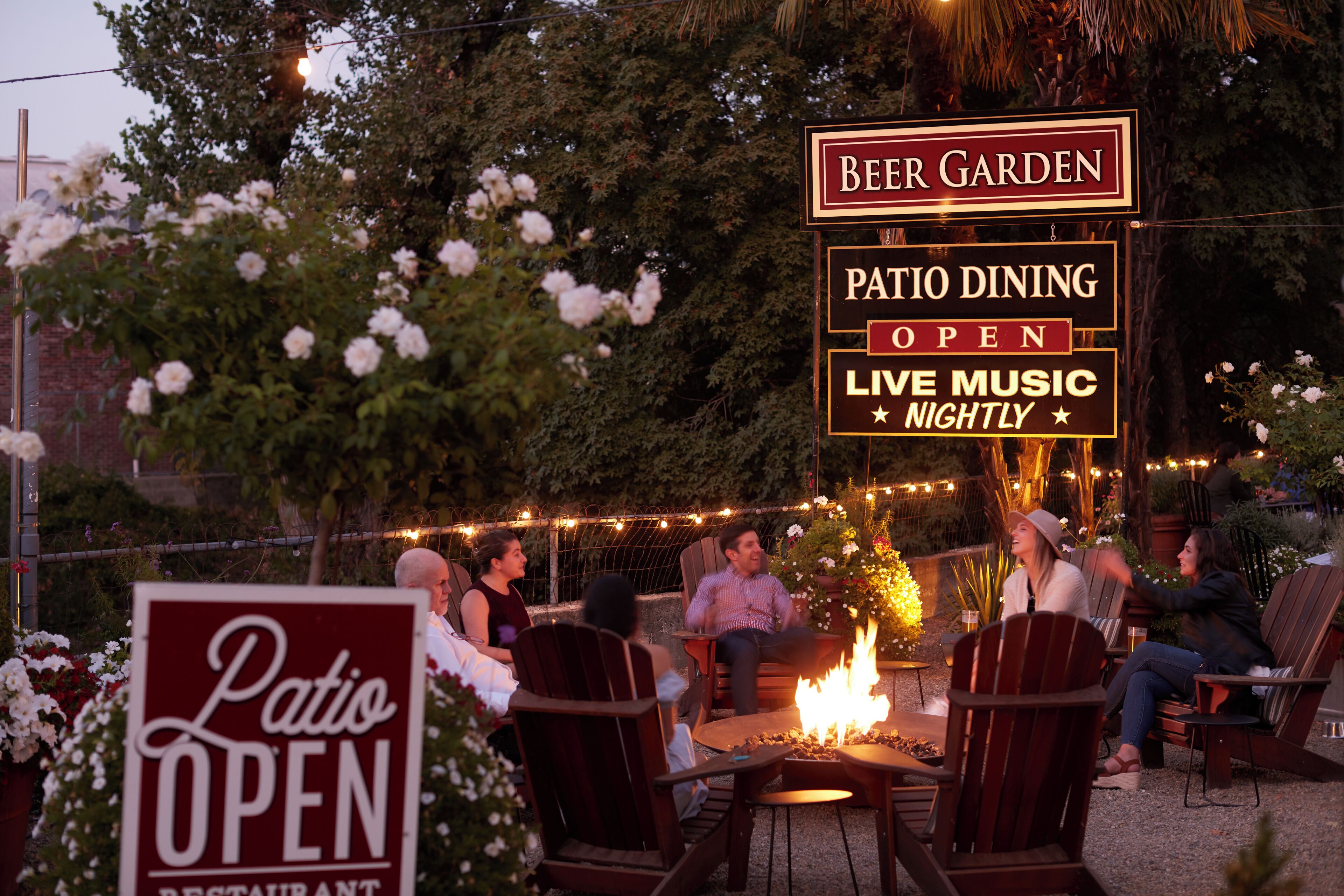 A patio dining area with chairs and a fire pit, surrounded by trees and string lights.