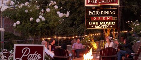 A patio dining area with chairs and a fire pit, surrounded by trees and string lights.