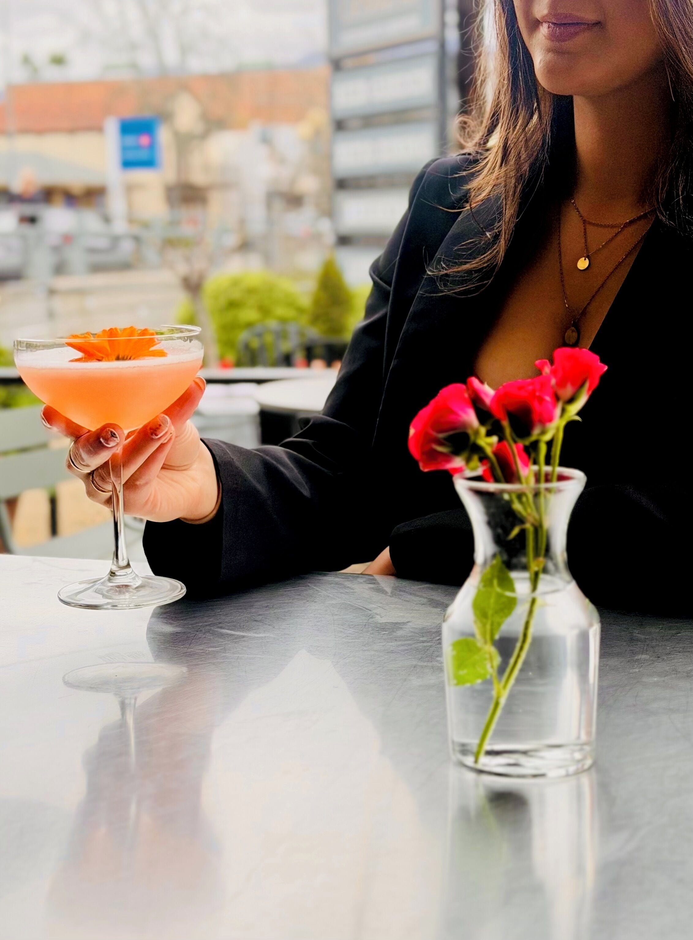 A person holding a cocktail with a garnish, sitting at a table with a vase of red roses.