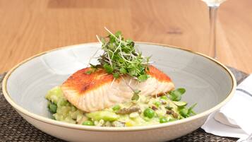 A bowl of food with a piece of fish on top, garnished with greens, and a glass of white wine in the background.