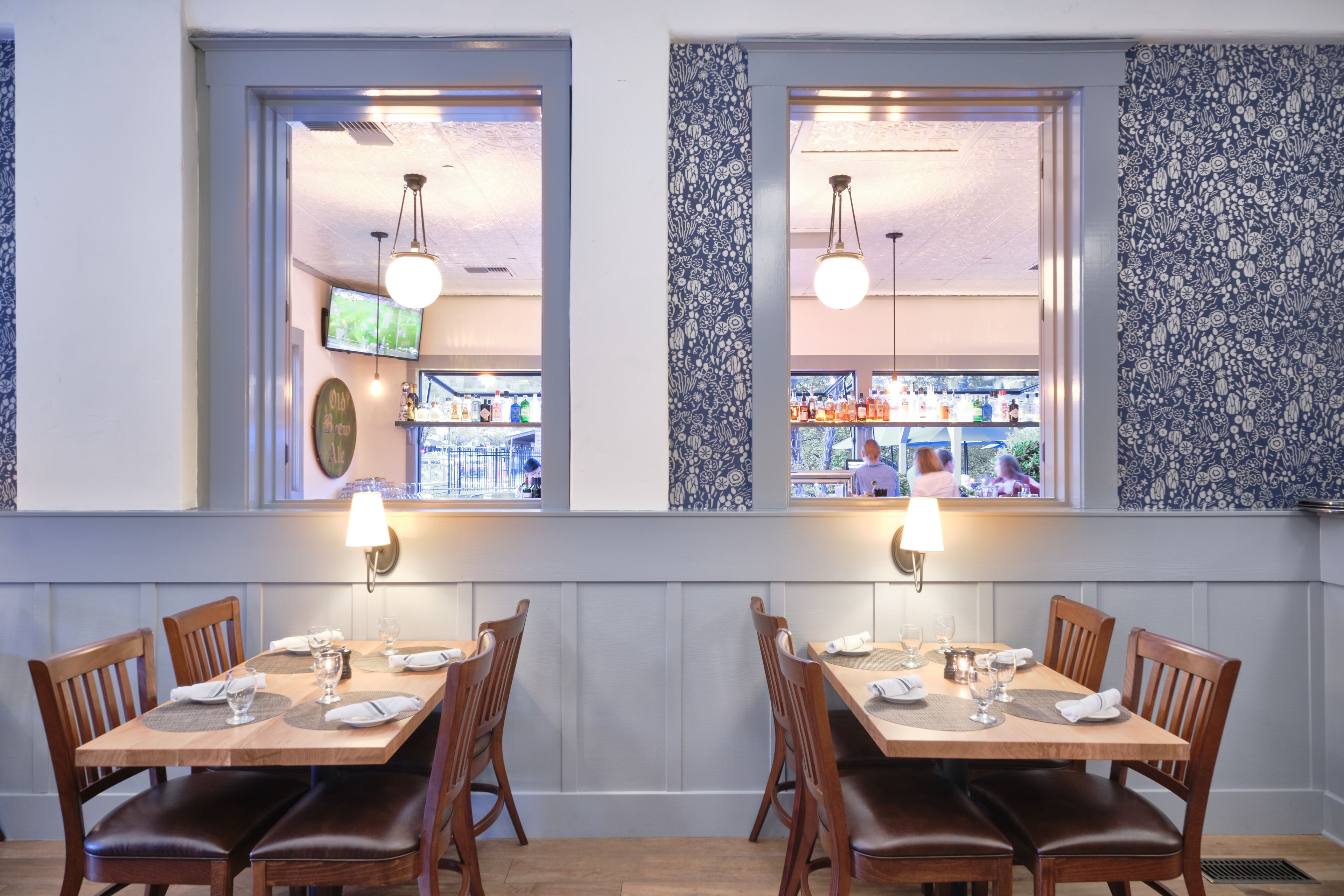 A restaurant with two dining areas, each with a wooden table and chairs, and a view of the street through large windows.