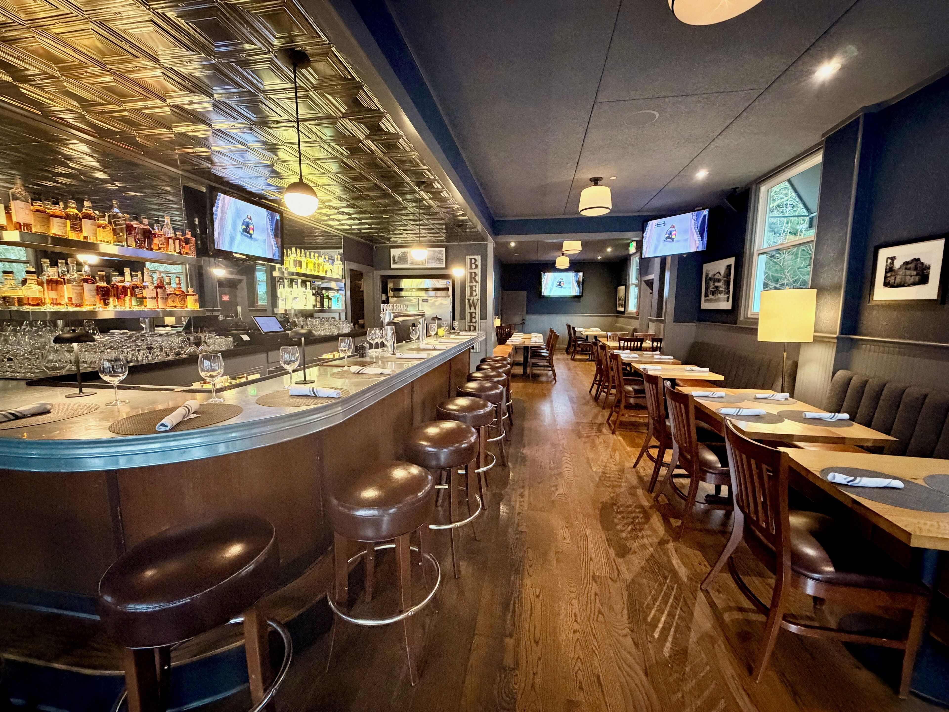 A bar area with stools, a counter with bottles, and a TV screen.