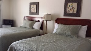 A hotel room with two beds, each with a wooden headboard, a bedside table, and a lamp. There are framed pictures on the wall.
